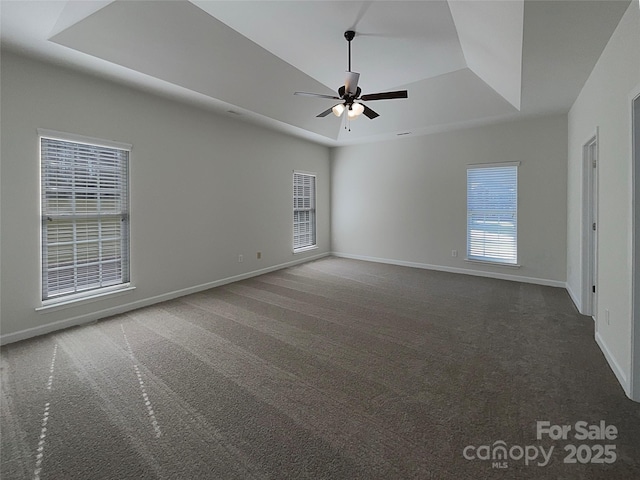 unfurnished room with ceiling fan, a tray ceiling, and dark colored carpet