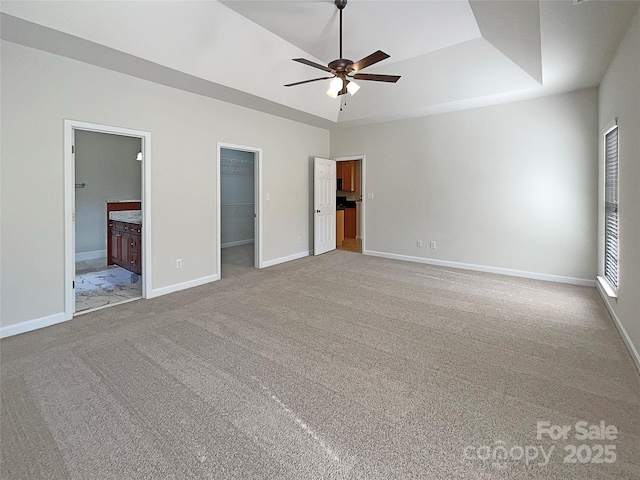 unfurnished bedroom featuring a raised ceiling, light carpet, a walk in closet, and connected bathroom