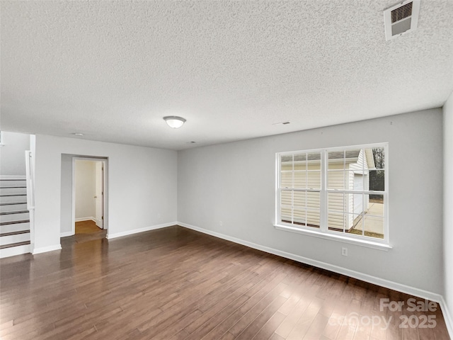 unfurnished room with dark wood-style flooring, visible vents, baseboards, and stairs