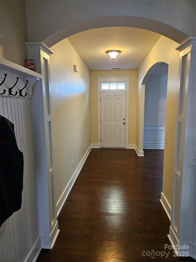 entryway with dark wood-type flooring, arched walkways, visible vents, and baseboards