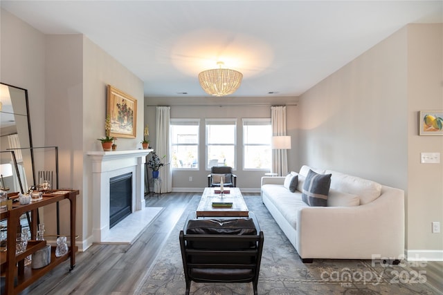 living room featuring a glass covered fireplace, an inviting chandelier, wood finished floors, and baseboards