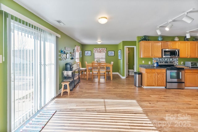 kitchen with appliances with stainless steel finishes, light hardwood / wood-style flooring, and decorative backsplash