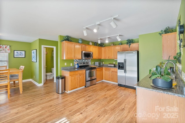 kitchen with light wood-type flooring, dark stone countertops, and stainless steel appliances