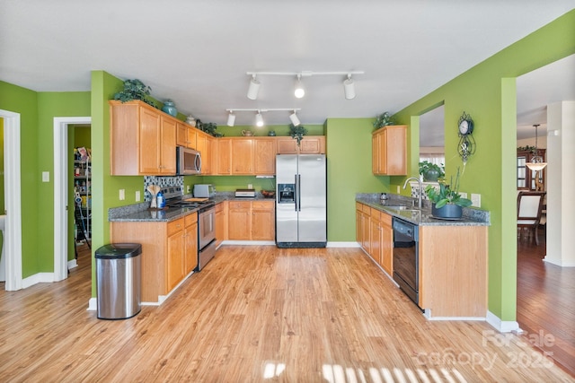 kitchen featuring appliances with stainless steel finishes, sink, dark stone counters, and light hardwood / wood-style flooring