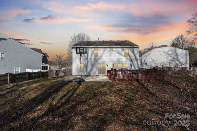 back house at dusk featuring a lawn, a patio, and a deck