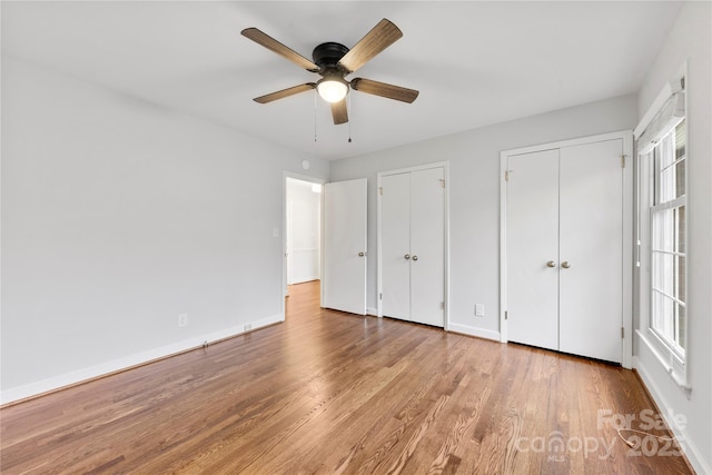 unfurnished bedroom featuring baseboards, two closets, a ceiling fan, and light wood-style floors