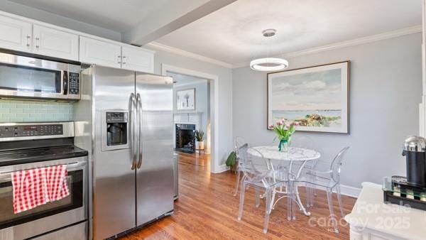 kitchen featuring light wood-style flooring, white cabinetry, crown molding, appliances with stainless steel finishes, and a fireplace