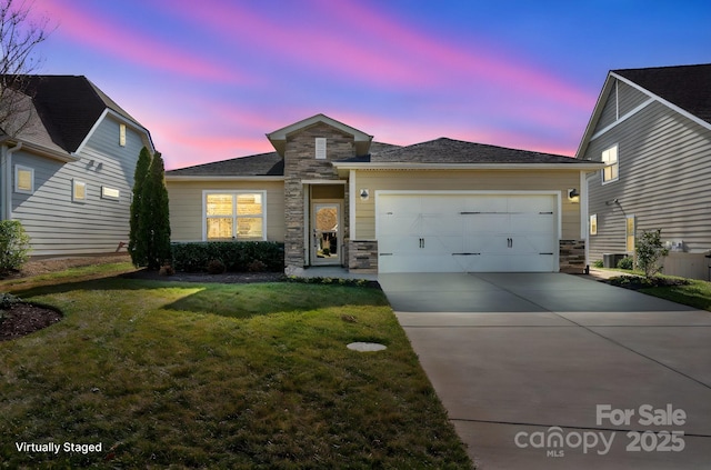 view of front of house with stone siding, a yard, an attached garage, and driveway