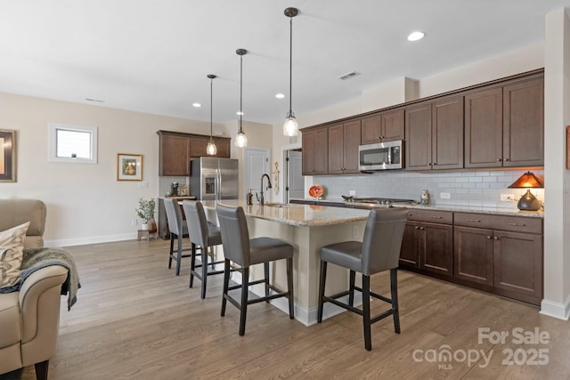 kitchen with stainless steel appliances, visible vents, light wood-style floors, decorative backsplash, and a kitchen bar