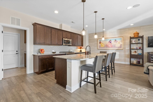 kitchen with visible vents, stainless steel microwave, a breakfast bar, light stone countertops, and a sink