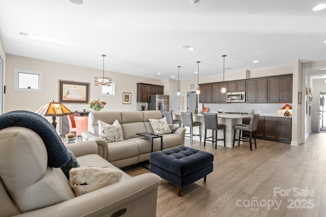 living room featuring a chandelier, recessed lighting, and light wood-style floors