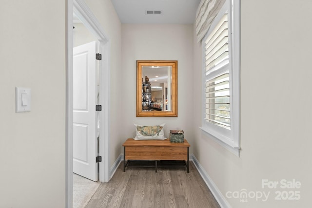 hall with light wood-type flooring, visible vents, and baseboards