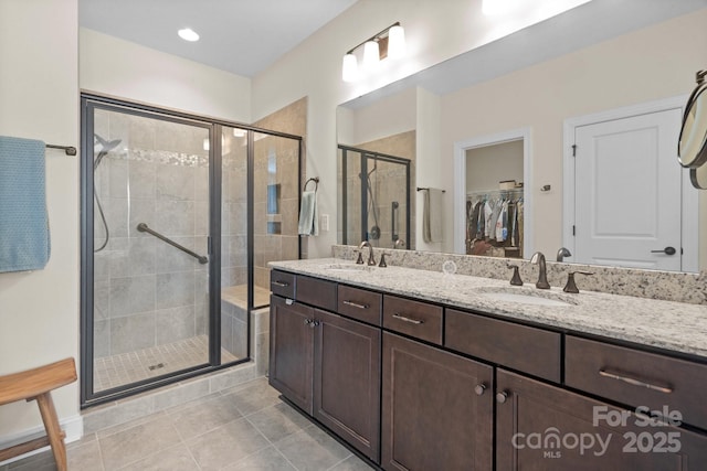 bathroom with a stall shower, a walk in closet, tile patterned flooring, and a sink