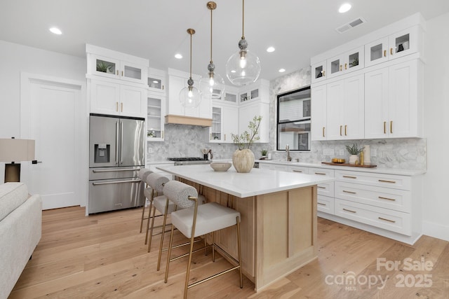 kitchen with light wood-type flooring, white cabinets, decorative light fixtures, a kitchen island, and high end refrigerator