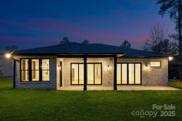 back house at dusk with a patio area and a lawn