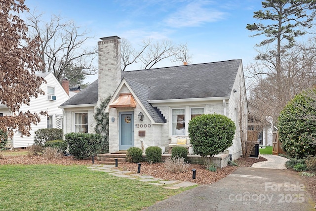 view of front of house featuring a shingled roof, brick siding, a chimney, and a front lawn