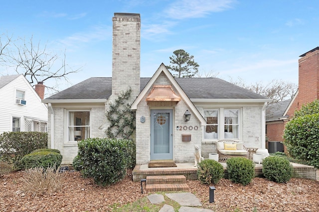 view of front of property with brick siding, a chimney, a shingled roof, and central air condition unit