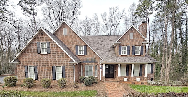 view of front facade featuring roof with shingles, a chimney, a porch, and brick siding