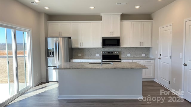 kitchen with stainless steel appliances, white cabinets, an island with sink, and light stone counters