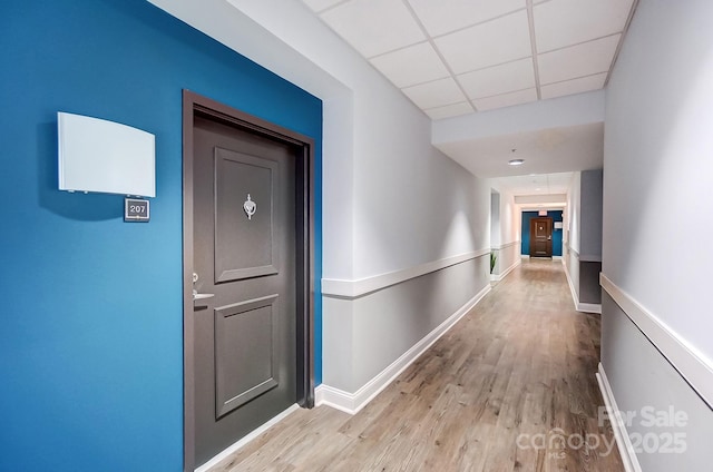 corridor with light wood-style floors, a paneled ceiling, and baseboards