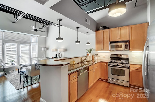 kitchen featuring decorative light fixtures, appliances with stainless steel finishes, open floor plan, a sink, and a peninsula