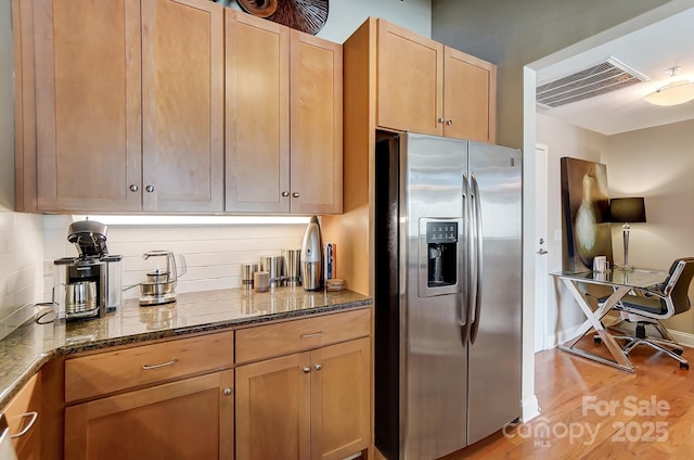 kitchen featuring dark stone counters, decorative backsplash, visible vents, and stainless steel fridge with ice dispenser