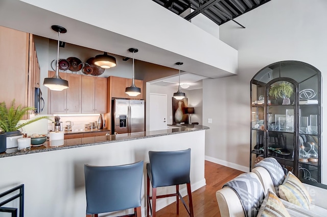 kitchen with stainless steel appliances, a peninsula, wood finished floors, dark stone countertops, and decorative light fixtures