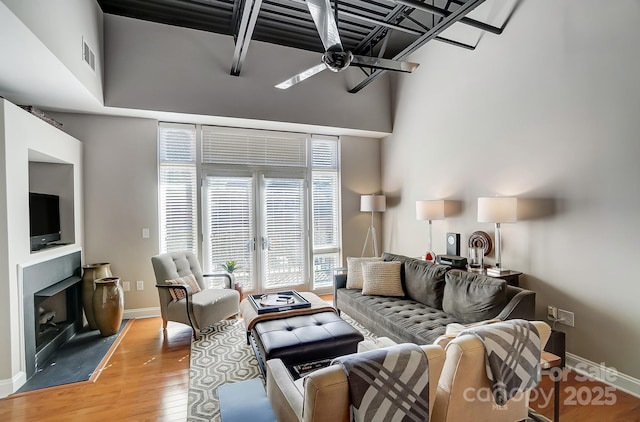 living room with visible vents, baseboards, light wood-style flooring, ceiling fan, and a fireplace with flush hearth