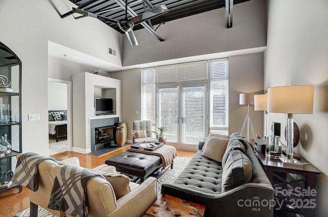 living area with a towering ceiling, light wood-style floors, and a fireplace with raised hearth