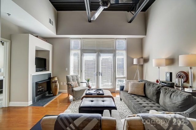 living area with a fireplace, visible vents, a towering ceiling, wood finished floors, and baseboards