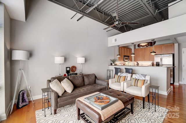 living room with visible vents, light wood-style flooring, a ceiling fan, and baseboards