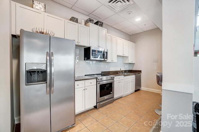 kitchen featuring white cabinets, dark countertops, appliances with stainless steel finishes, a sink, and light tile patterned flooring