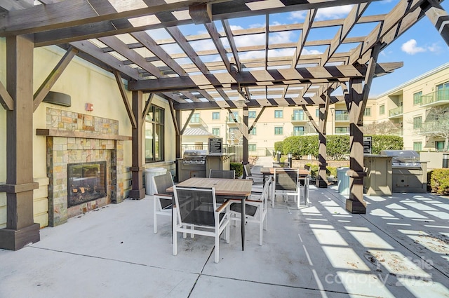 view of patio with outdoor dining area, an outdoor kitchen, grilling area, a pergola, and a glass covered fireplace