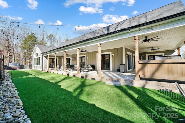 rear view of property with board and batten siding, a yard, a patio, and a ceiling fan