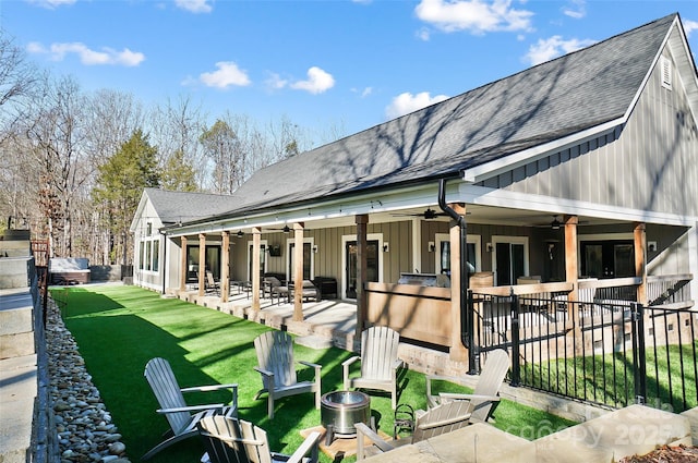 rear view of property featuring a lawn, a ceiling fan, a patio, roof with shingles, and board and batten siding