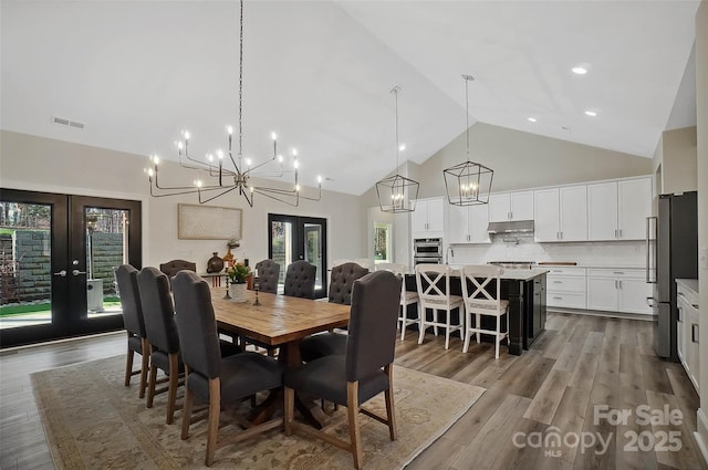 dining space with french doors, a chandelier, visible vents, wood finished floors, and high vaulted ceiling