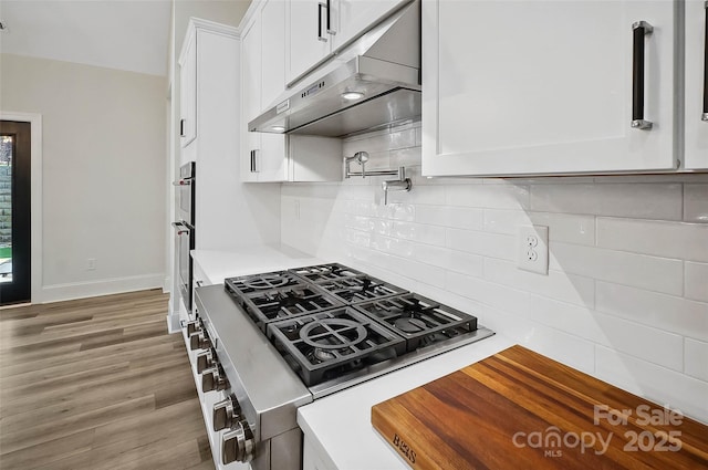 kitchen featuring dark wood finished floors, light countertops, decorative backsplash, white cabinets, and under cabinet range hood