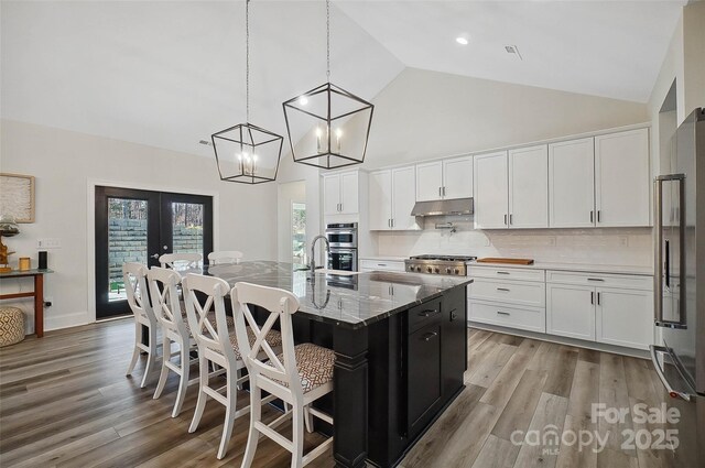 kitchen featuring under cabinet range hood, stainless steel appliances, white cabinetry, a center island with sink, and decorative light fixtures