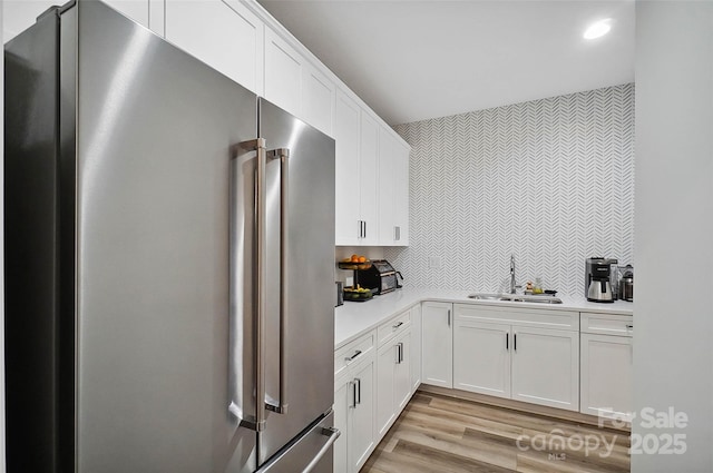 kitchen featuring white cabinets, light countertops, a sink, and high end refrigerator