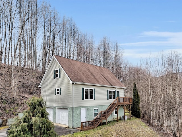 exterior space featuring aphalt driveway, a shingled roof, a garage, a wooden deck, and stairs