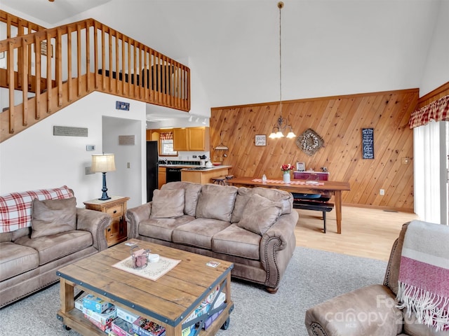 living room featuring wooden walls, a high ceiling, stairway, and a notable chandelier