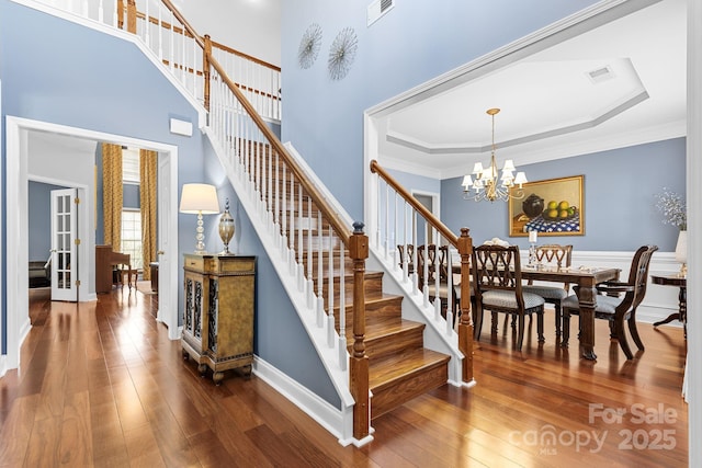 stairway with hardwood / wood-style flooring, ornamental molding, a raised ceiling, and a notable chandelier