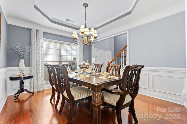 dining space featuring ornamental molding, a notable chandelier, wood-type flooring, and a raised ceiling