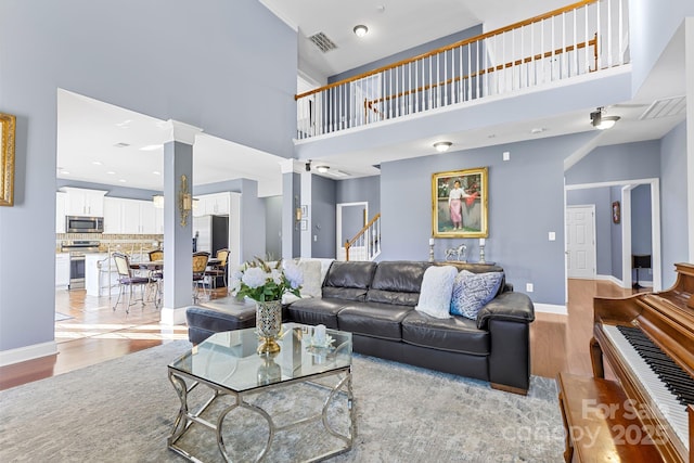 living room with light hardwood / wood-style flooring, ornate columns, and a towering ceiling