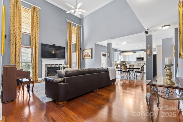 living room featuring ceiling fan, dark wood-type flooring, a towering ceiling, and a stone fireplace