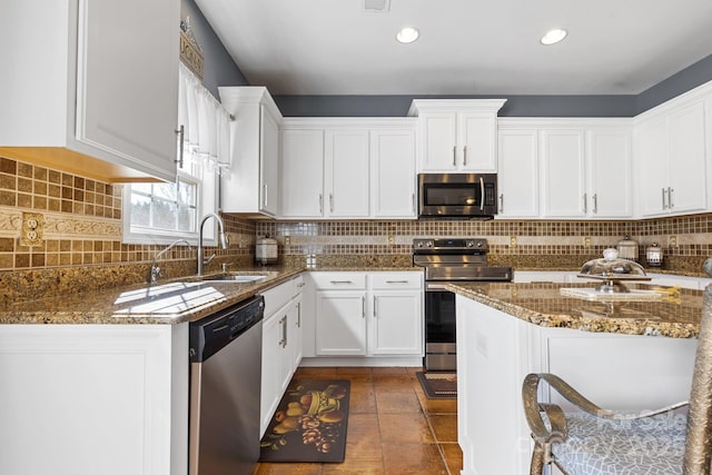 kitchen with stainless steel appliances, decorative backsplash, sink, white cabinetry, and dark stone countertops