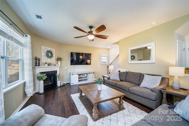 living room featuring a glass covered fireplace, wood finished floors, visible vents, and a healthy amount of sunlight