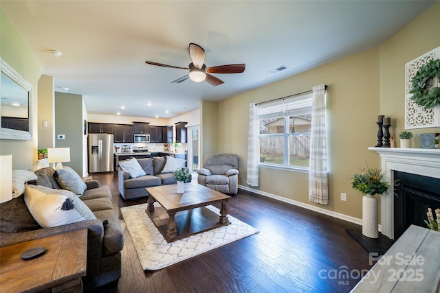 living area featuring recessed lighting, a fireplace with raised hearth, dark wood-type flooring, ceiling fan, and baseboards