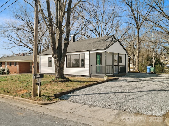 view of front of home featuring driveway, a porch, crawl space, and a chimney