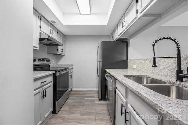 kitchen with light stone countertops, baseboards, a sink, under cabinet range hood, and appliances with stainless steel finishes